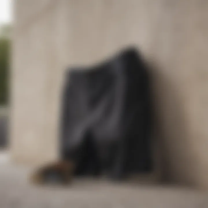 Close-up of plain black shorts with skateboard propped against a wall.